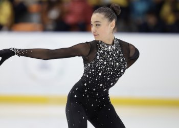 Annika Chao in a bedazzled black body suit, looks to the left over her arm as she skates.