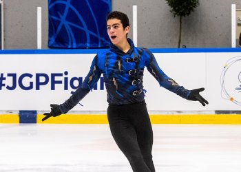 Jacob Sanchez, with his arms out to the side while he skates, an excited look on his face. Taken from the thigh up, he wears black pants and a blue and black top.
