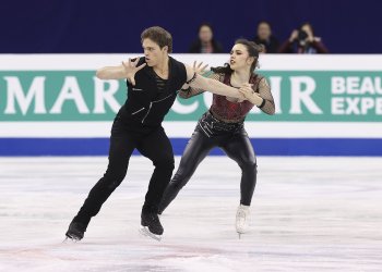 Michael Parsons, dressed in all black, and Caroline Green, dressed in black leather and a fishnet top with a red undershirt, skate closely together, showing their chemistry.