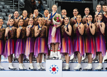 The Haydenettes stand on the podium, each athlete holding up their silver medal. They wear their free skate costumes, which are purple with red and orange hues. 