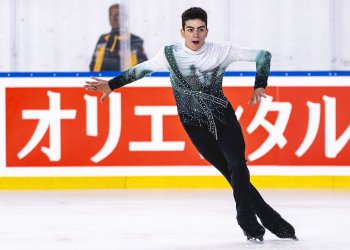 Jacob Sanchez skates forward his arms out to the side. He wears black pants and a white, green and black top.
