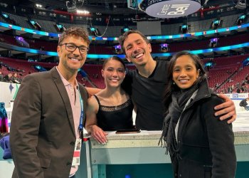 Valentina Plazas and Maximiliano Fernandez stand at the boards, their arms wrapped about their coaches (Jim Peterson left) and Amanada Evora Will (right). They all smile, the rink in the background.