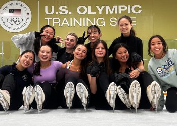 A group of female skaters pose for a photo on the ice on front of a sign that says "U.S. Olympic Training Site"