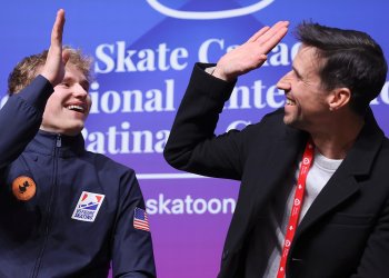 Ilia Malinin, left, high-fives his coach and father in the kiss and cry after the skater's world record breaking free skate.