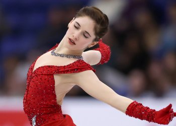Isabeau Levito, wearing a red dress and red gloves, displays her emotion as she leans back with arms extended.