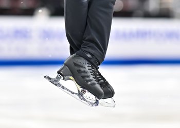 Closeup of a pair of black skates. The skater is wearing black pants