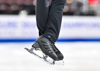 close up photo of a male skater's black skates. You can see the skater is wearing black pants. 