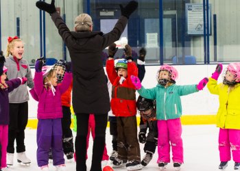 Several young skaters give a big smile with their arms up on the ice