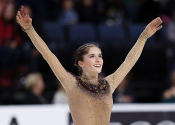 Isabeau Levito, wearing a light brown colored dress with a snake on it, raises her arms as she salutes the crowd.