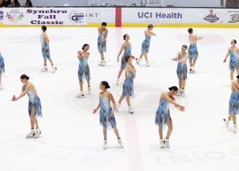 The Lexettes hit their starting pose, spread out across the ice in a circle, for their short program. They wear dresses with different blues.