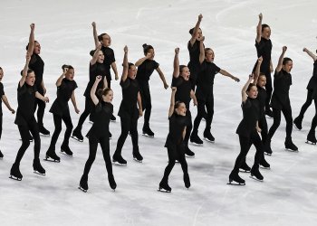 Skaters stand with one arm raised eith smiles on their faces. They are all wearing matching black costumes