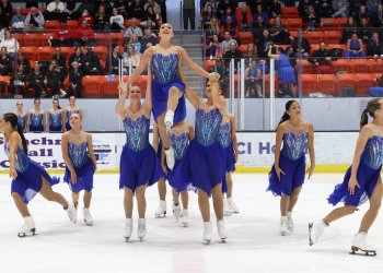 Miami University competes in their free skate. The team is wearing matching blue and purple skating costumes. In the middle, two skaters hold a teammate up in the air.