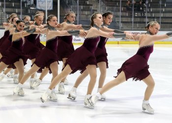 The Northernettes skate together holding each other by the shoulders in matching dark red skating costumes