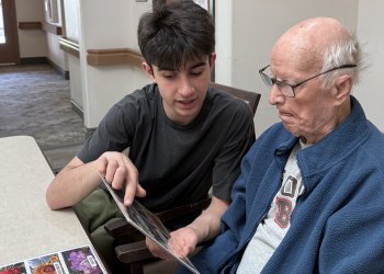 Ryan Azadpour, dressed in a black shirt, points to photographs as his grandfather with Alzheimer's looks on.