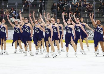 The Skyliners in purple dresses, stand together with each holding their right arm up in the air.