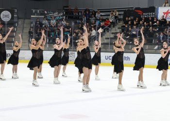 The Starlights junior synchro team skates in unison with their arms reaching upwards wearing matching black skating costumes