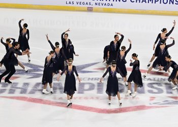  The Haydenettes, in black dresses with purple detail down the front and back, hit a pose at center ice, the left side mirroring the right.