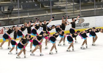 Teams Elite in black dresses with bright underlay perform on the ice in unison.