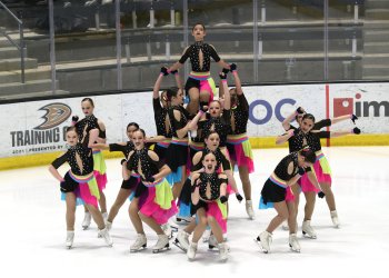 Teams Elite in black and hot pink dresses in a group with one skater lifted high above.