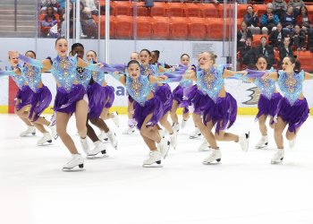 Team Image, in dresses with purple skirts and light blue with purple accents on top, skate in lines of four. 