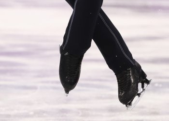 Black figure skates performing a jump on ice.