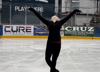 A skater poses on the ice with her arms outstretfhed