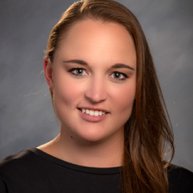 Headshot of a Caucasian woman smiling. She has long brown hair and is wearing a black shirt 