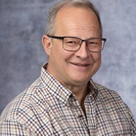 Headshot of Mitch Moyer. He is a Caucasian man with grey hair. He is wearing a plaid shirt and glasses 
