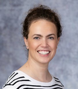 Headshot of Julie Parkes. She is a Caucasian woman with brown curly hair worn up in a bun. She is wearing a black and white striped shirt 
