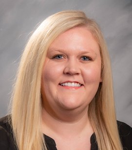 Headshot of a Caucasian woman smiling. She has long blonde hair and is wearing a black shirt.