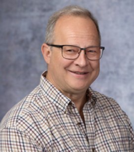Headshot of Mitch Moyer. He is a Caucasian man with grey hair. He is wearing a plaid shirt and glasses 