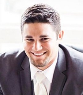 Headshot of Pat Bloemen. He is a Caucasian ma with short black hair. He is wearing a black suit and white tie 