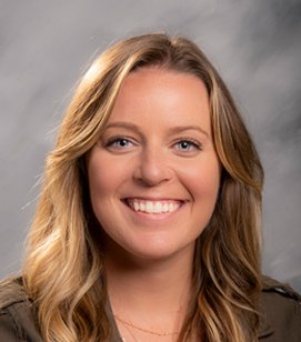 Headshot of a Caucasian woman smiling. She has blonde hair and she is wearing a brown shirt